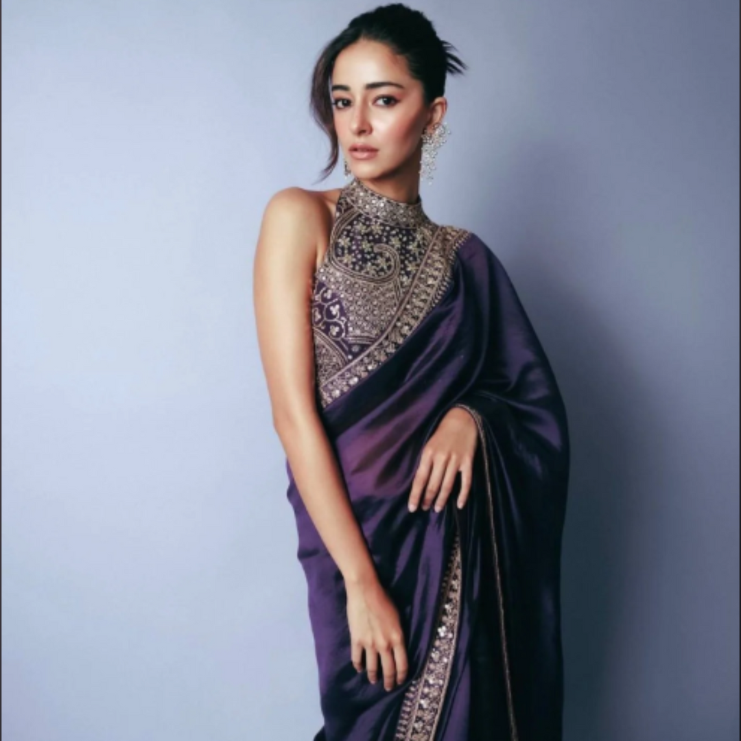 Woman wearing a purple saree with intricate designs against a gray background