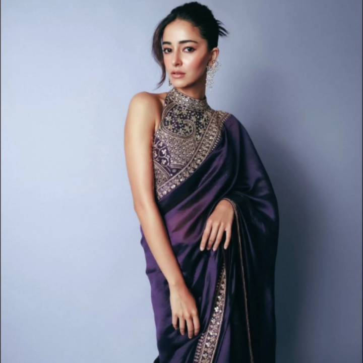 Woman wearing a purple saree with intricate designs against a gray background