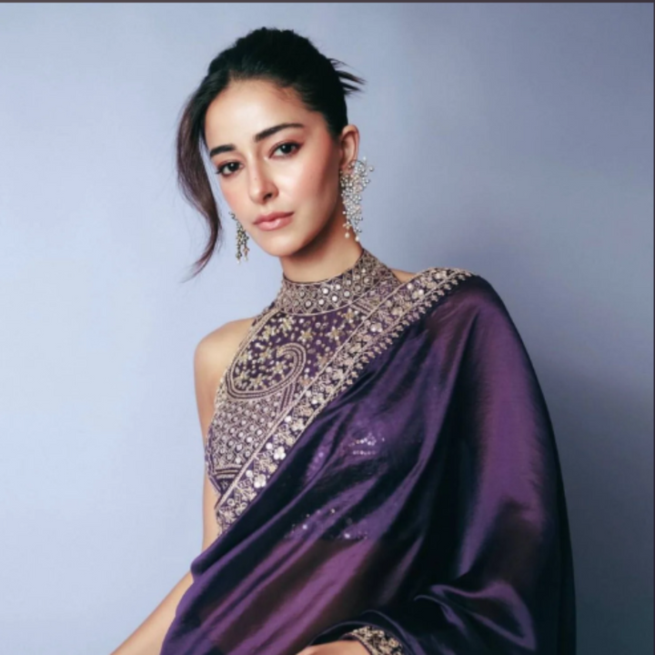 Woman wearing a purple saree with intricate designs against a light blue background