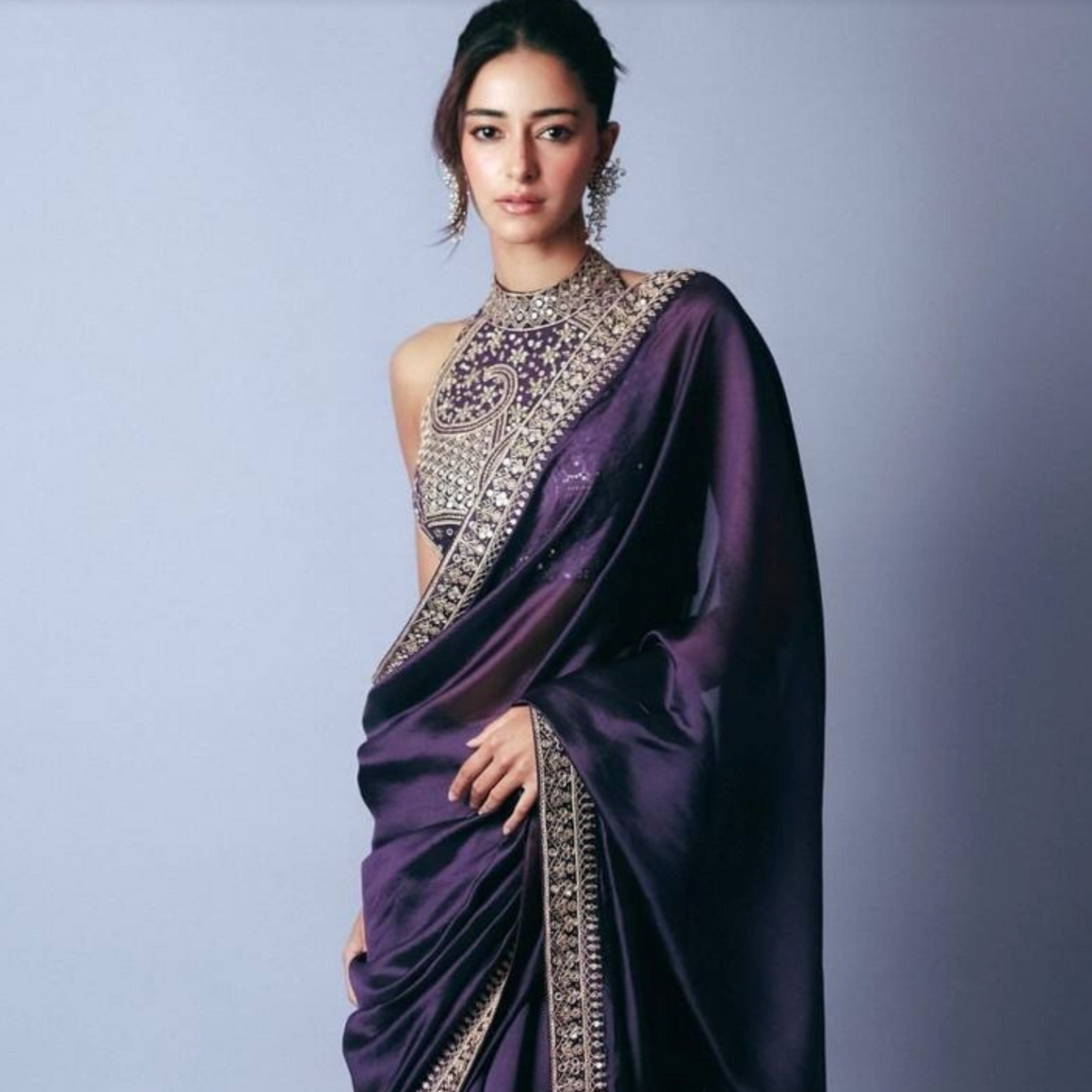 Woman wearing a purple saree with intricate gold patterns on a light purple background