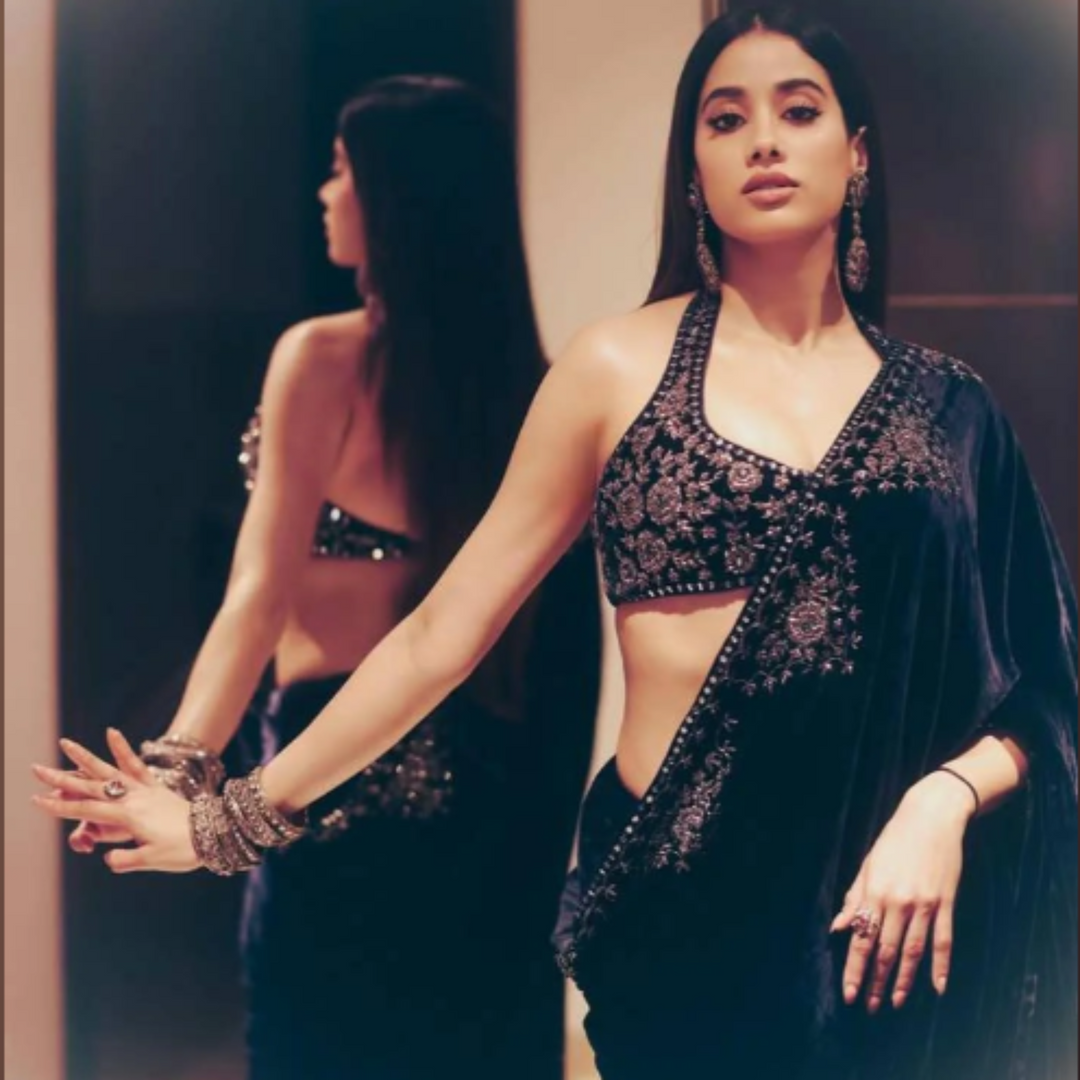 Woman in a black saree with intricate patterns standing in front of a mirror.
