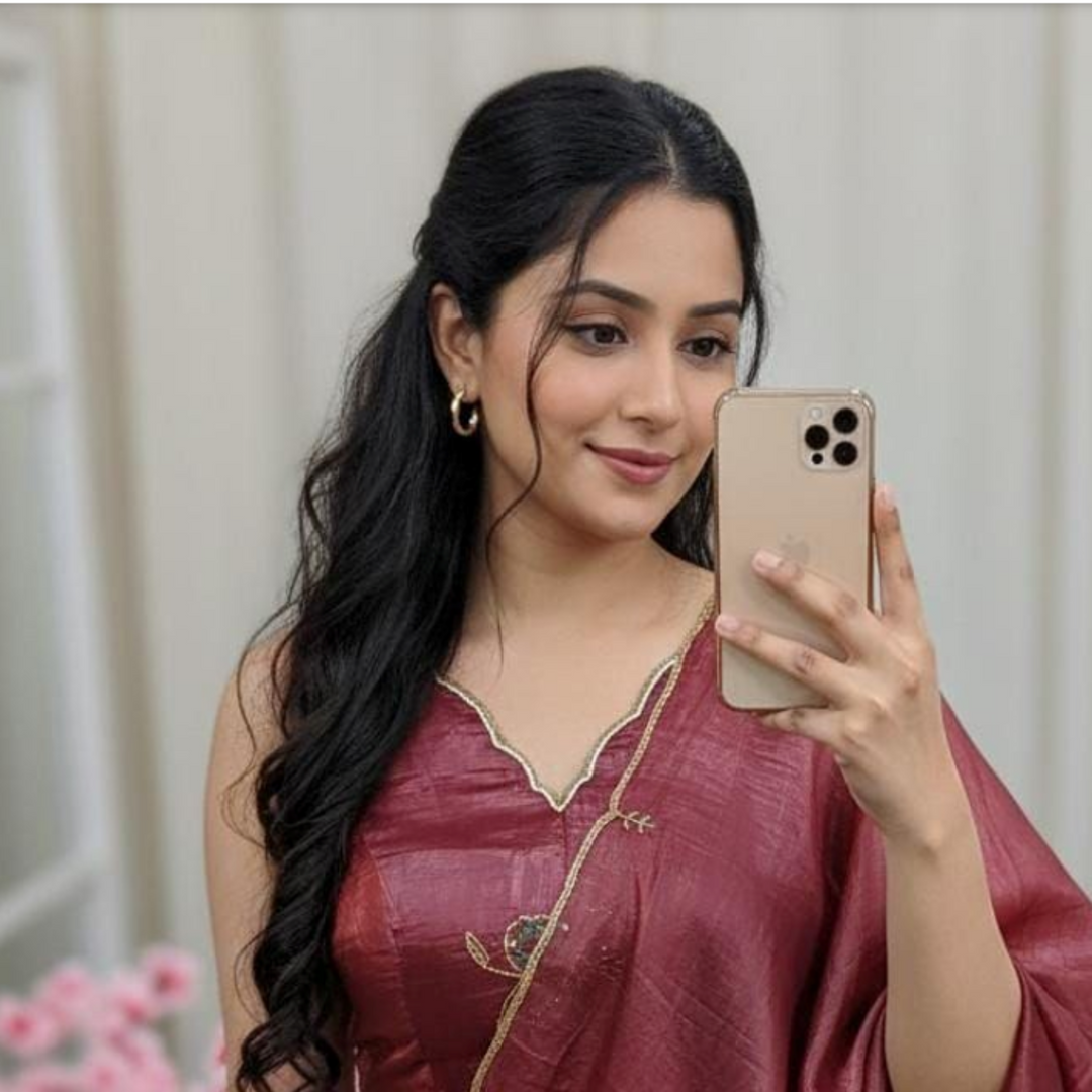 Woman in a maroon saree taking a mirror selfie with a smartphone.