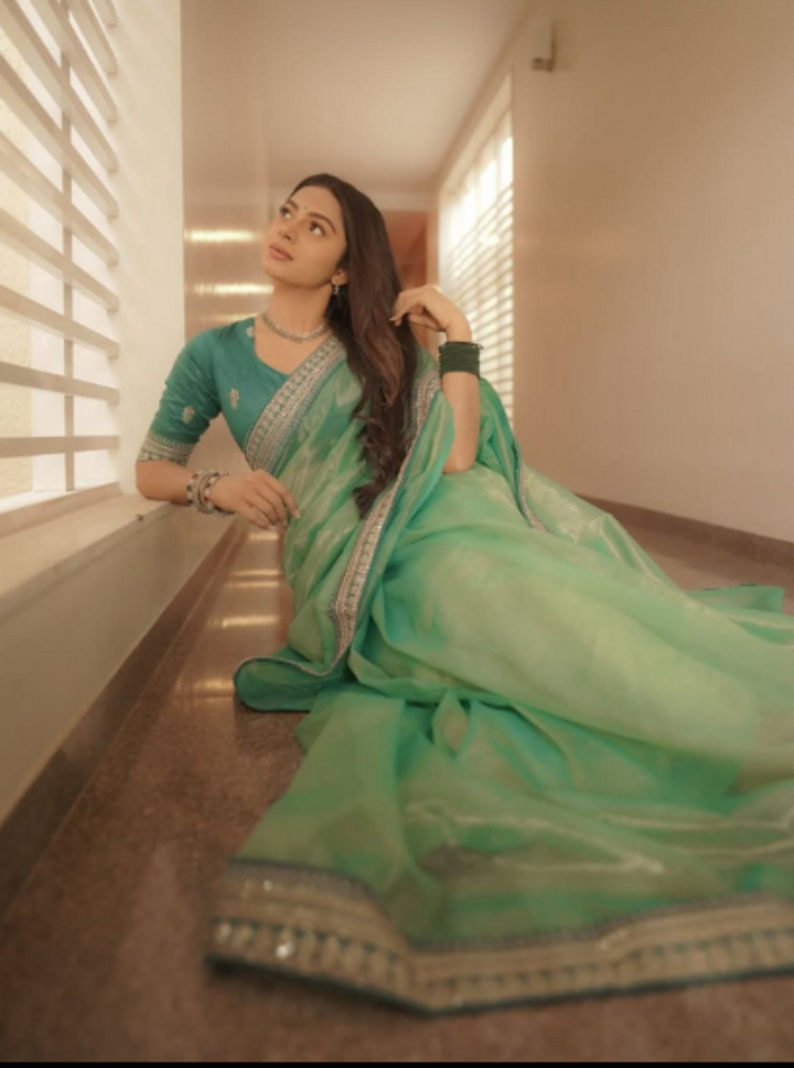 Woman in a teal saree sitting on a floor with a neutral background
