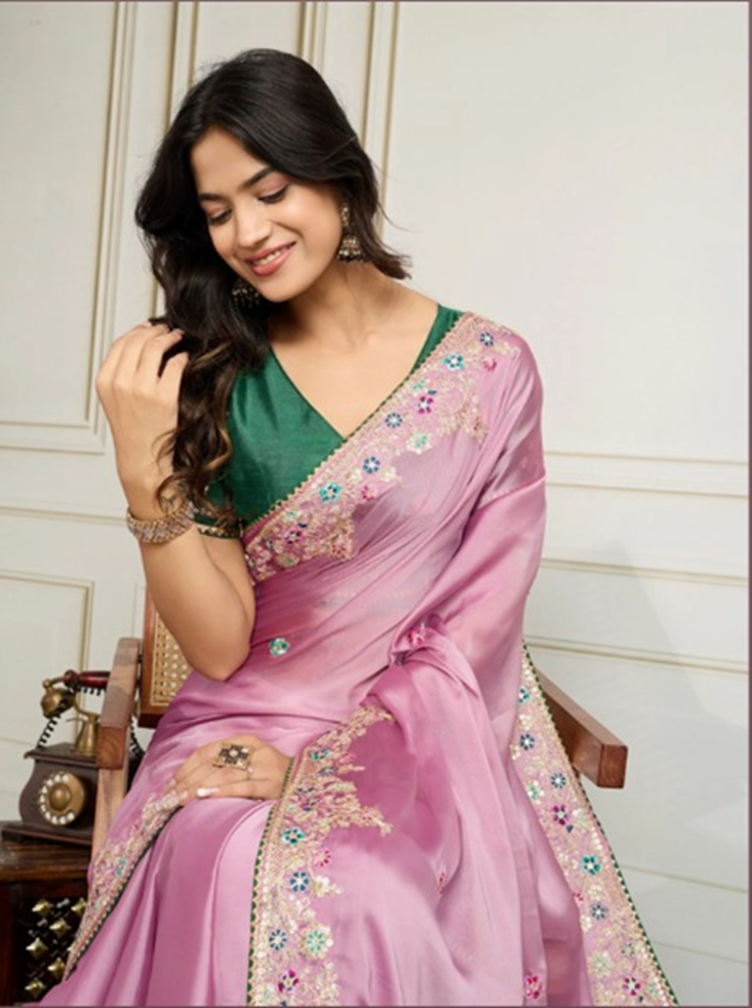Woman wearing a pink saree with green blouse, sitting on a chair.